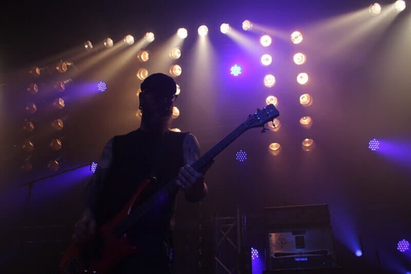 Musiker, der auf der Bühne E-Gitarre spielt, beleuchtet von hellen Scheinwerfern und violettem Umgebungslicht.