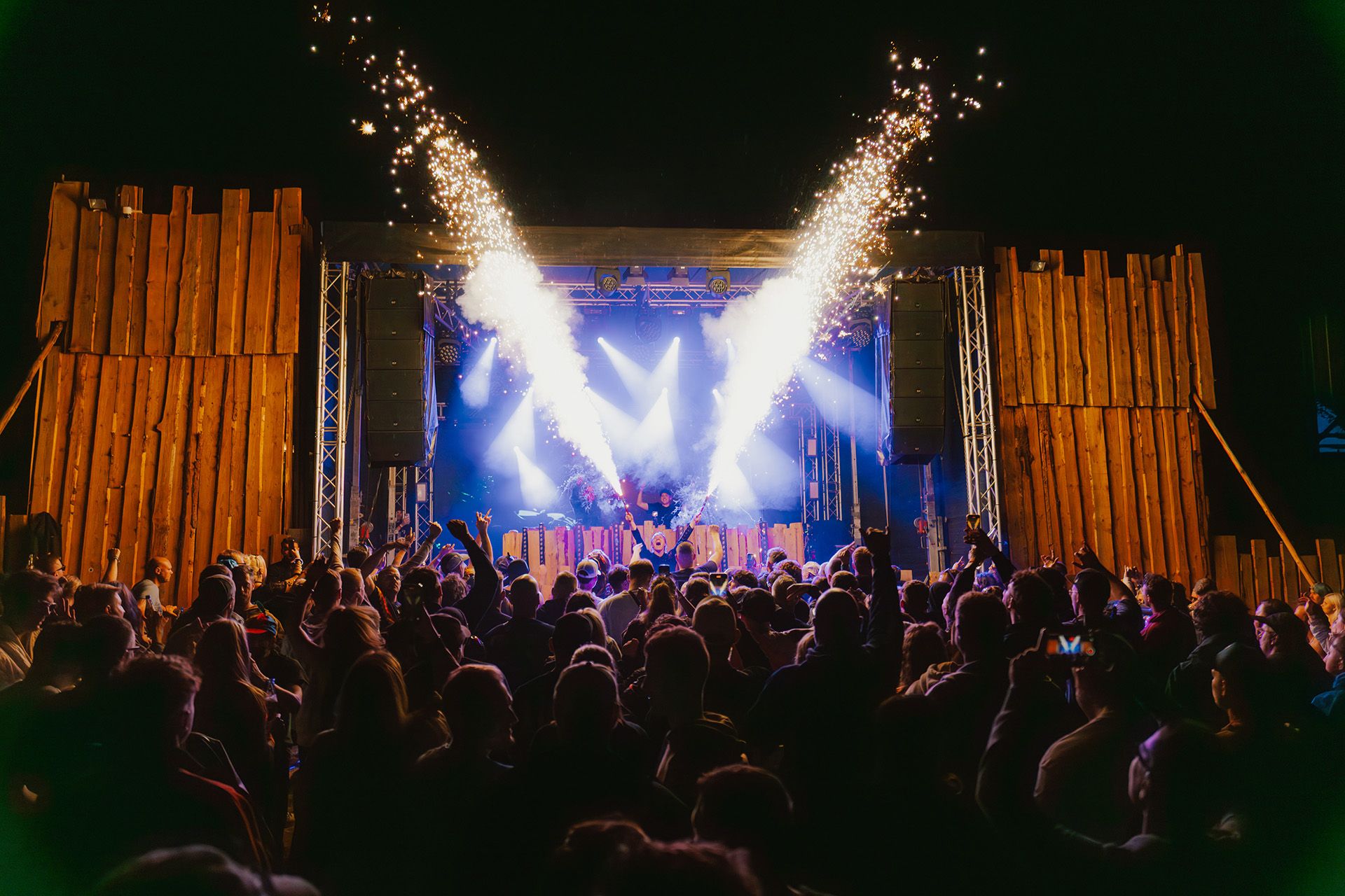 Eine lebhafte Menschenmenge feiert ein Konzert, während spektakuläre Feuerwerke explodieren.
